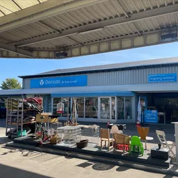 Blauwe gevel van kringloopwinkel met naam Dorcas zichtbaar, onder afdak met spullen uitgestald op het terras