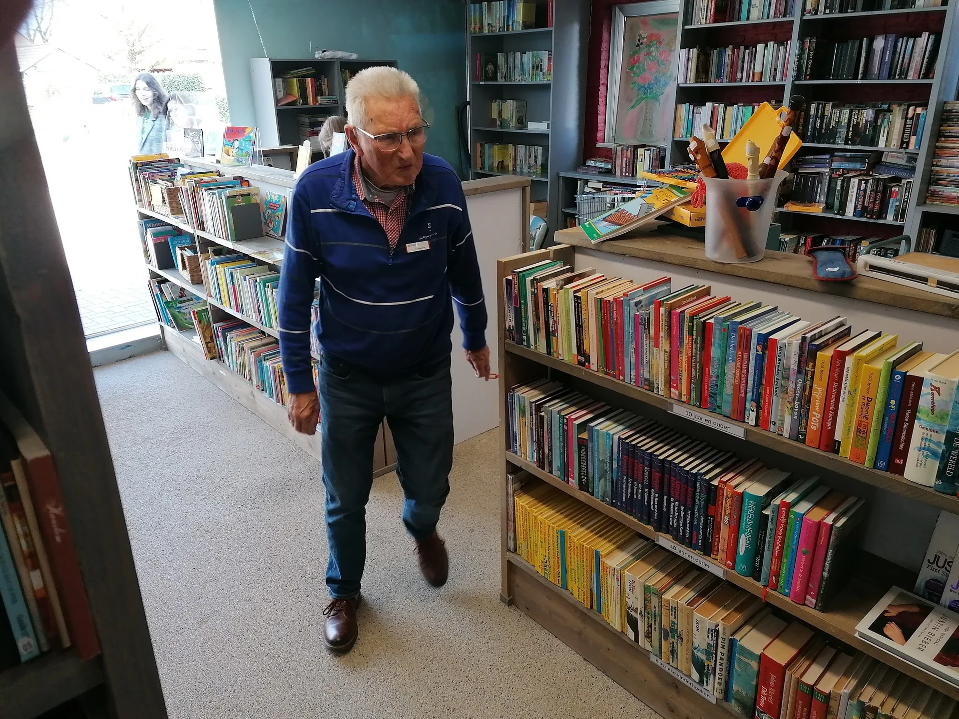 Oudere man loopt door boekenafdeling met volle boekenkasten aan beide zijden in kringloopwinkel