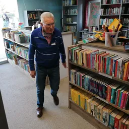 Oudere man loopt door boekenafdeling met volle boekenkasten aan beide zijden in kringloopwinkel