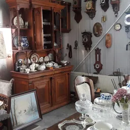 Houten buffetkast met porselein, servies en decoratieve items; aan de muur horloges en diverse antieke spullen
