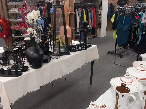 Winkelvloer met kledingrekken, uitgestalde serviesgoed en decoratieve items op tafels