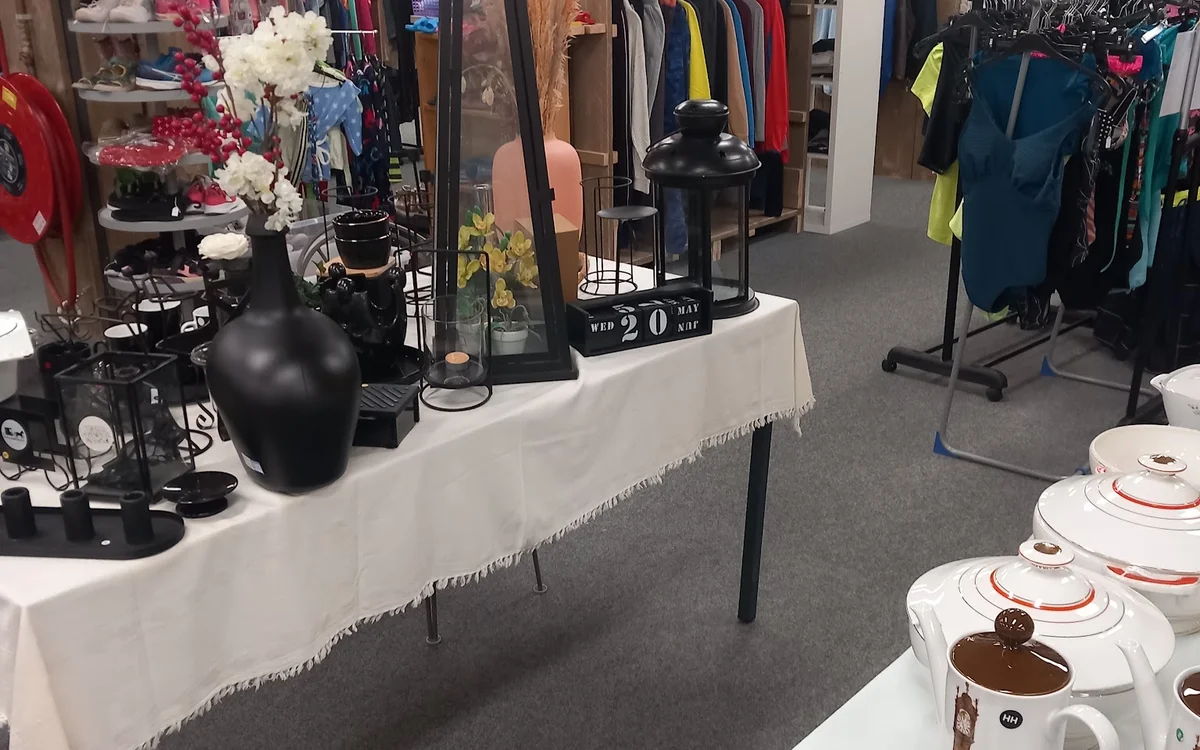 Winkelvloer met kledingrekken, uitgestalde serviesgoed en decoratieve items op tafels