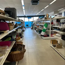 Winkelinterieur met stellingen vol spullen langs beide zijden en een breed middenpad met heldere verlichting