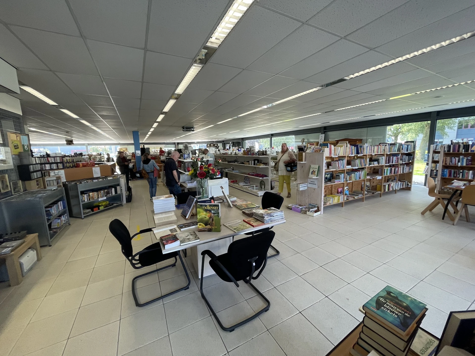 Overzicht van de winkelvloer met boekenkasten, tafels met stoelen en bezoekers tussen de stellingen