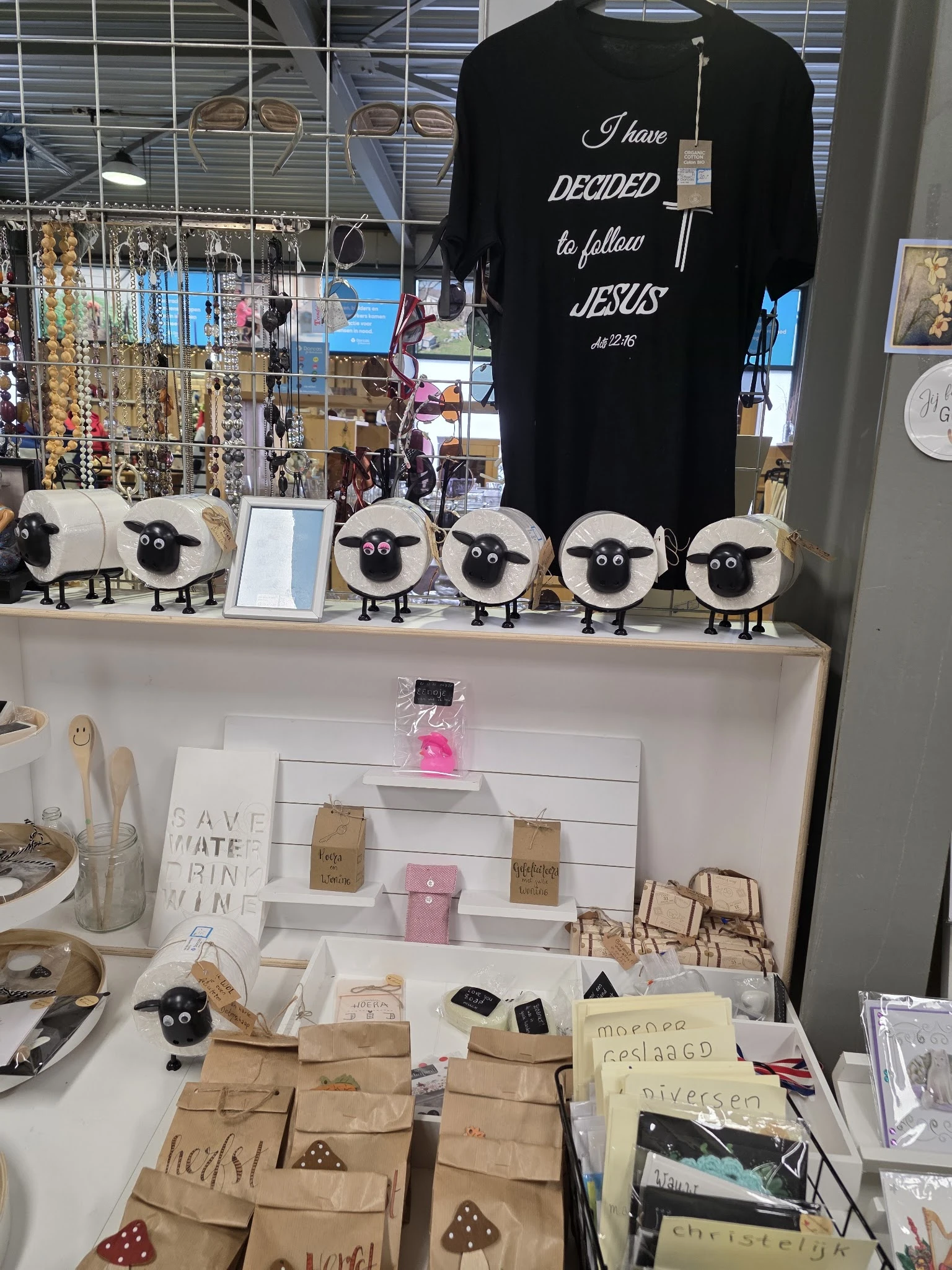 Uitstalling met decoratieve schapen-figuren, sieraden, kaarten en handgemaakte items op een witte tafel in de winkel