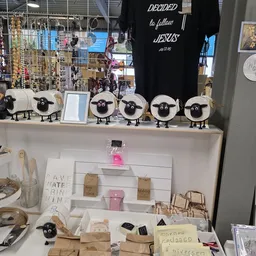 Uitstalling met decoratieve schapen-figuren, sieraden, kaarten en handgemaakte items op een witte tafel in de winkel