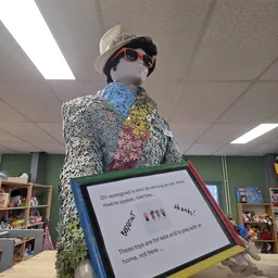 Mannequin gekleed in een zilveren glitterjas met gekleurde vlakken, met hoed en zonnebril, in een winkelinterieur.