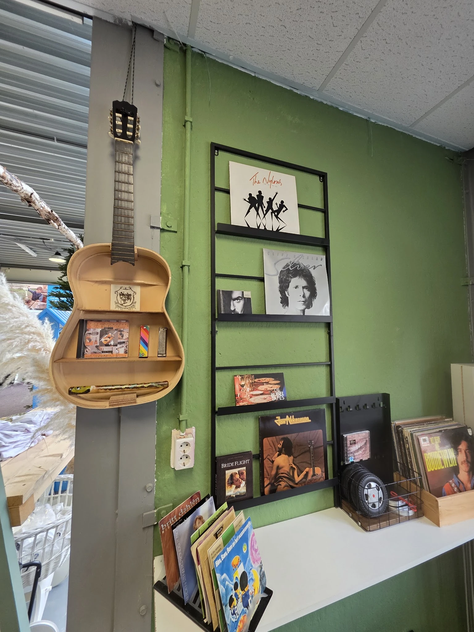 Gitaar-vormige wandplank met verzameling vinylplaten, cd's en muziekposters op groene muur