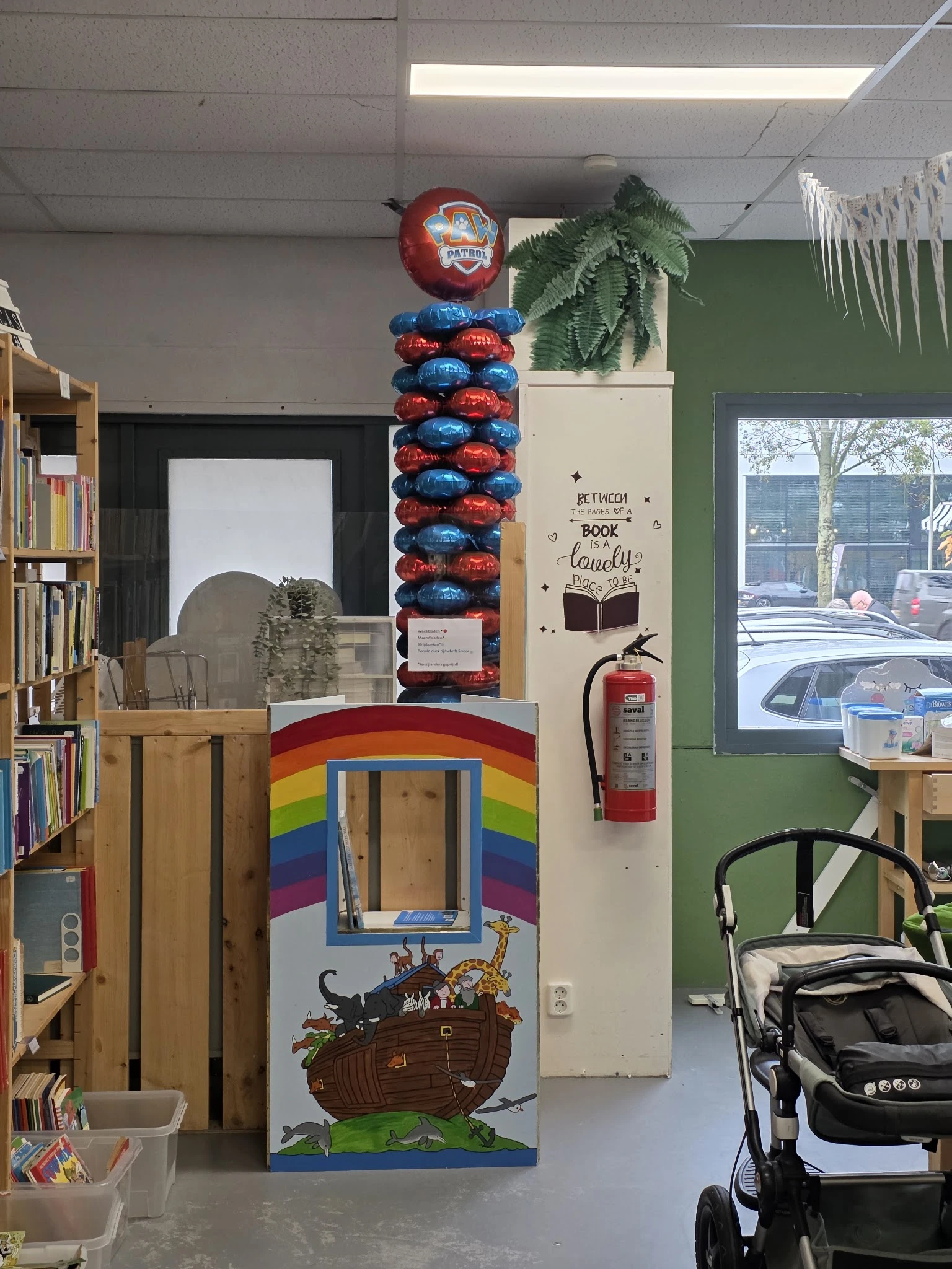 Winkelvloer met boekenkasten, regenboogbeschilderde speelkast, rode extinguisher en decoraties aan wand