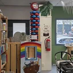 Winkelvloer met boekenkasten, regenboogbeschilderde speelkast, rode extinguisher en decoraties aan wand