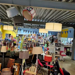 Winkelvloer met stellingen, kleding, meubels en lampen; gele muren en bunting-versiering
