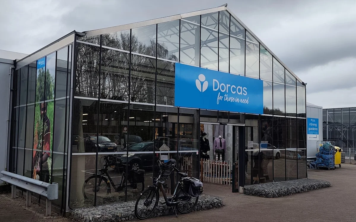 Moderne gevel van Dorcas kringloopwinkel met grote ramen, blauwe naam bord en fietsen buiten