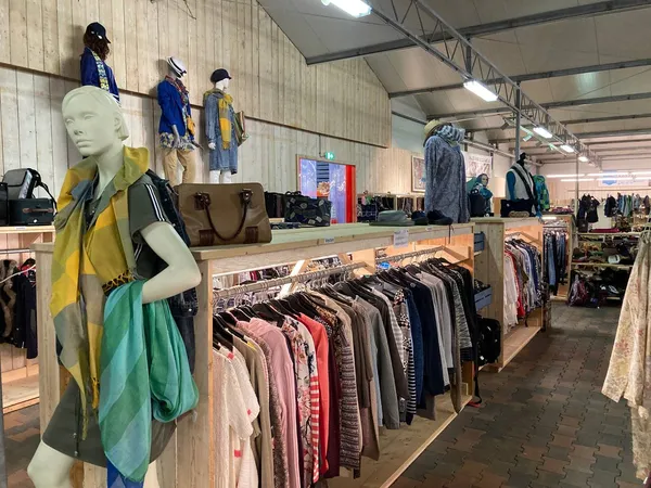 Winkelinterieur met kledingrekken, mannequins met kleding en tassen op houten displaytafels