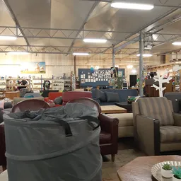 Ruim winkelbinnenruimte met diversen meubels, stoelen en banken uitgestald onder industriële plafondconstructie