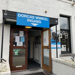Gevel van kringloopwinkel met blauwe entree, houten deuren en uithangbord met winkelnaam