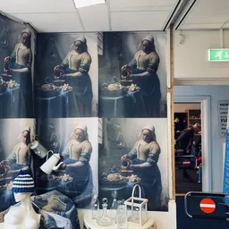 Winkelinterieur met grote kunstdrukken aan de muur en spullen op tafels, groene nooduitgang zichtbaar