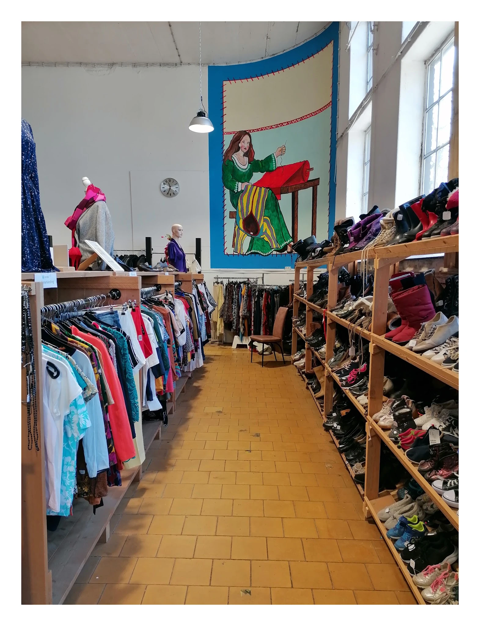 Winkelinterieur met houten stellingen vol tweedehands kleding, schoenen en accessoires langs de wanden