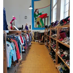 Winkelinterieur met houten stellingen vol tweedehands kleding, schoenen en accessoires langs de wanden