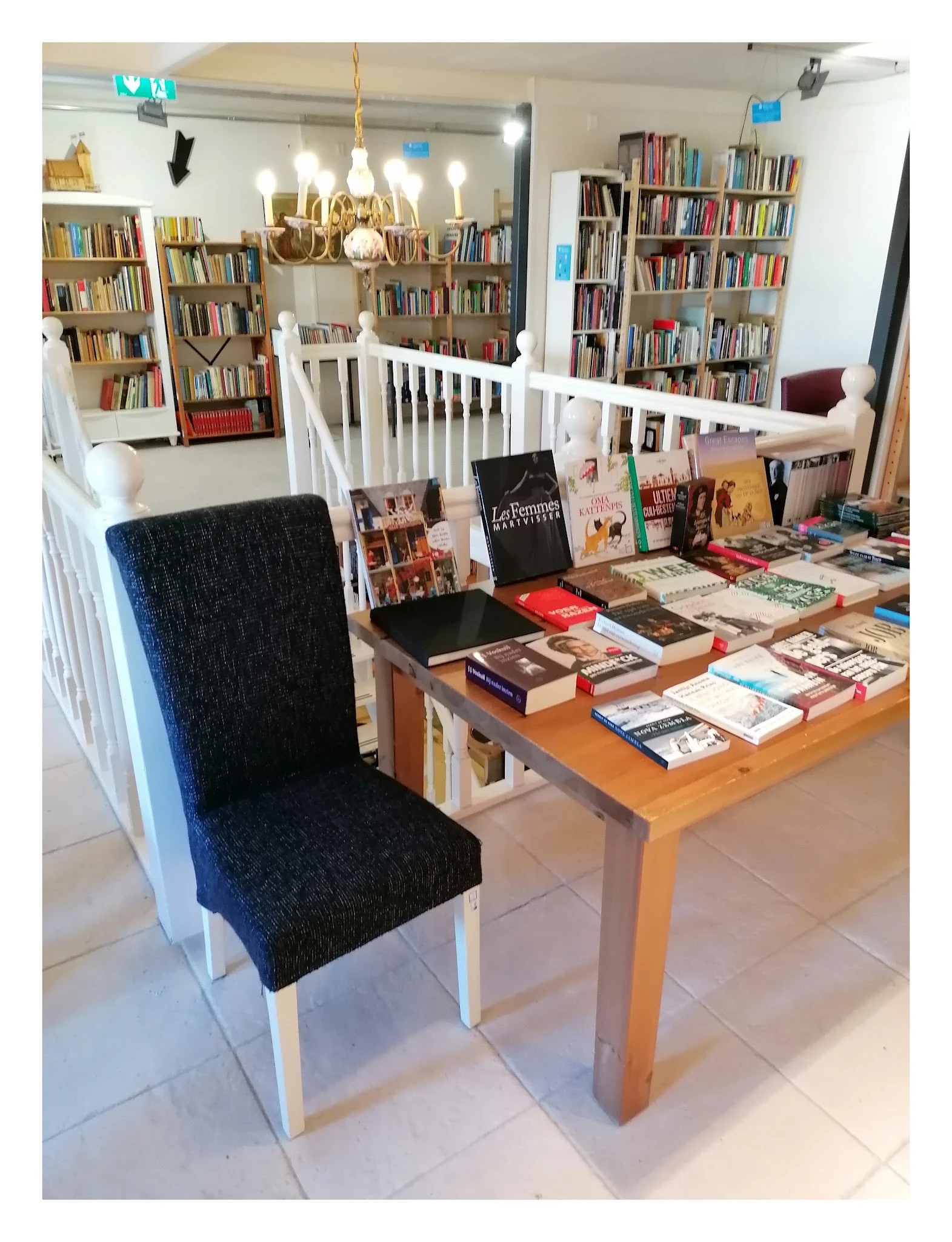 Houten tafel vol uitgestalde boeken en ander readingmateriaal in een kringloopwinkel, met boekenkasten op de achtergrond