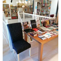 Houten tafel vol uitgestalde boeken en ander readingmateriaal in een kringloopwinkel, met boekenkasten op de achtergrond