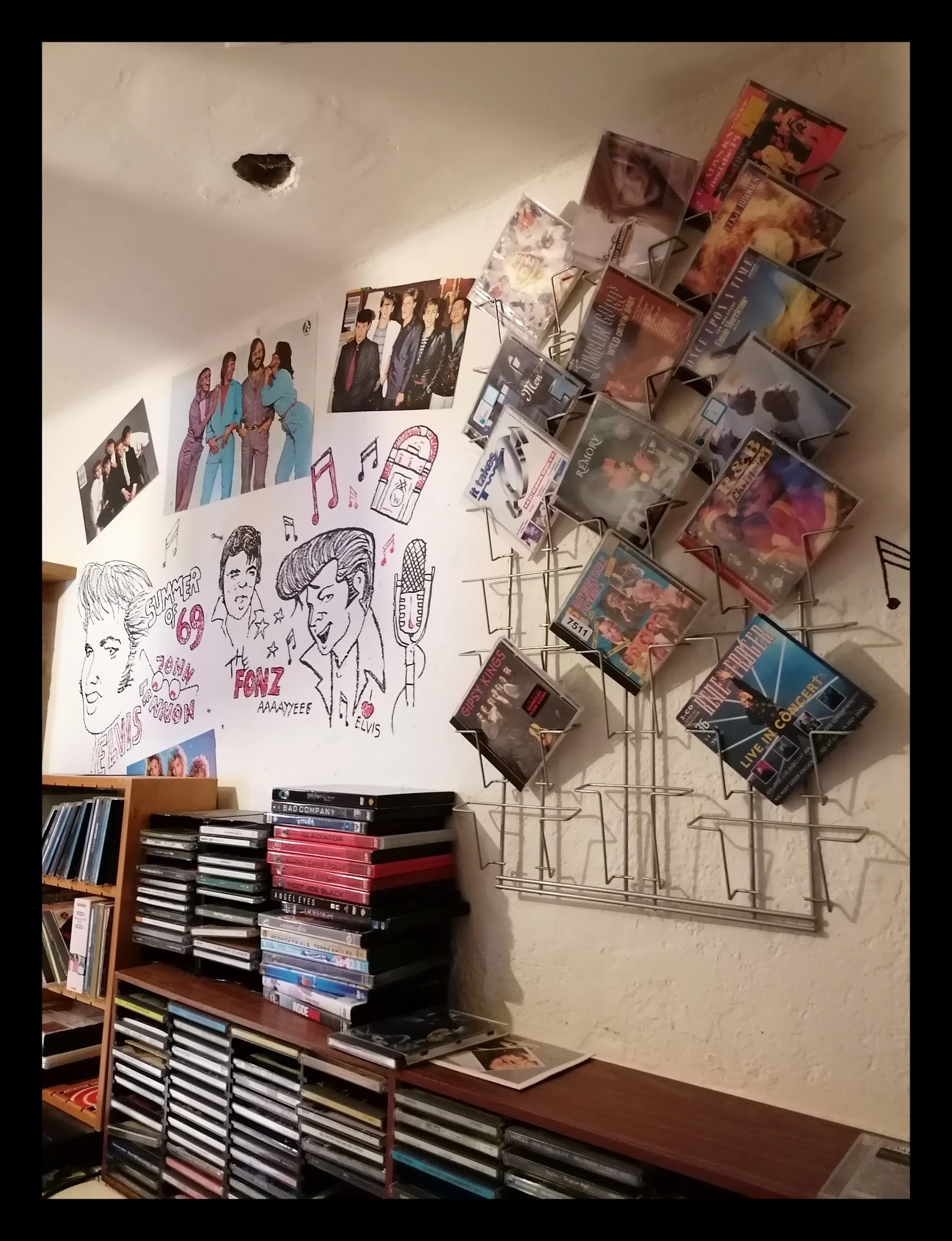 Muurwand met uitgestalde cd's, dvd's, foto's en handgeschreven posters in een kringloopwinkel