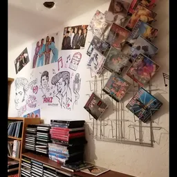 Muurwand met uitgestalde cd's, dvd's, foto's en handgeschreven posters in een kringloopwinkel