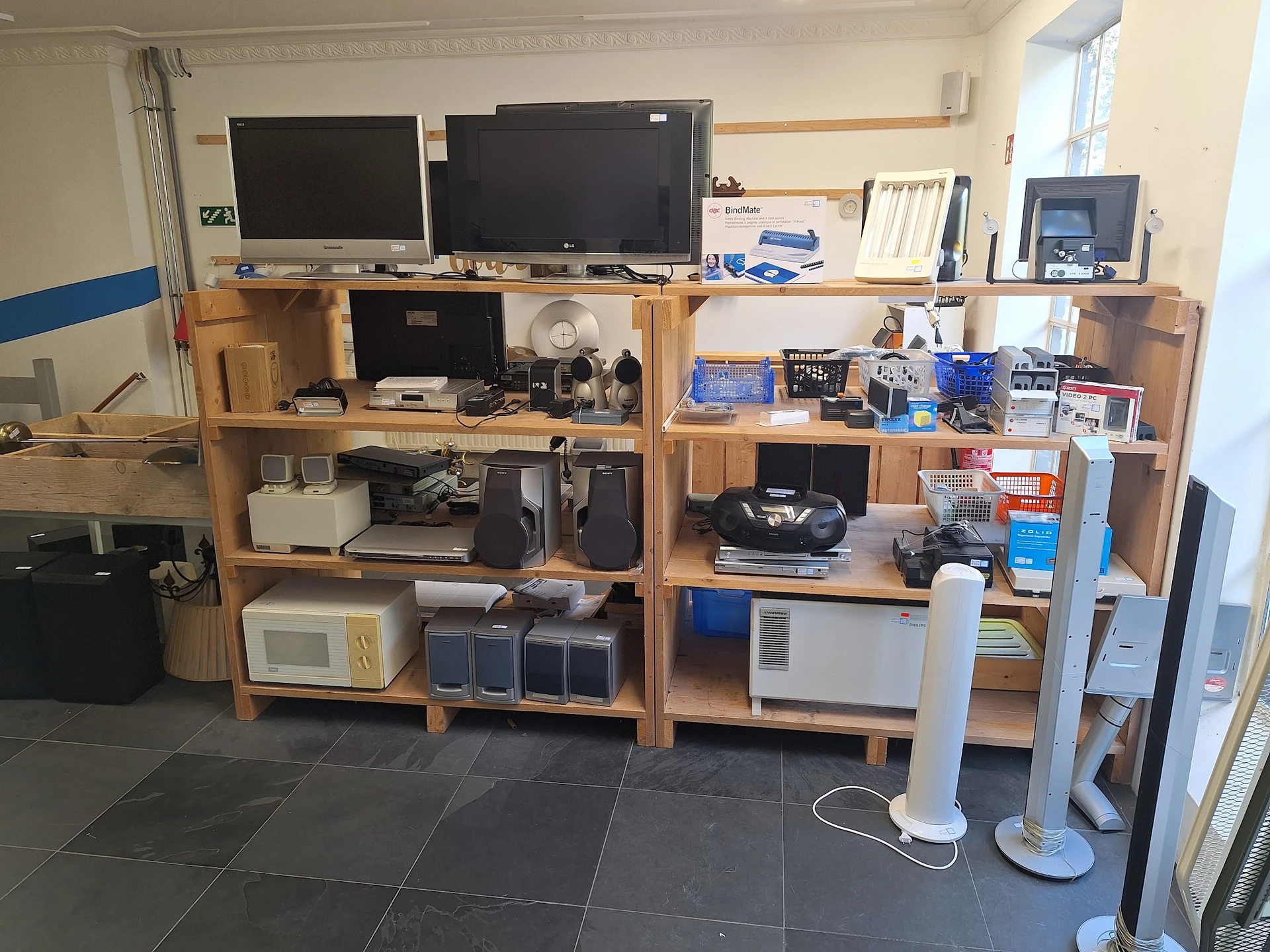 Houten stellingen met elektronische apparaten, televisies en huishoudelijke spullen in een kringloopwinkel