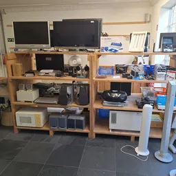 Houten stellingen met elektronische apparaten, televisies en huishoudelijke spullen in een kringloopwinkel