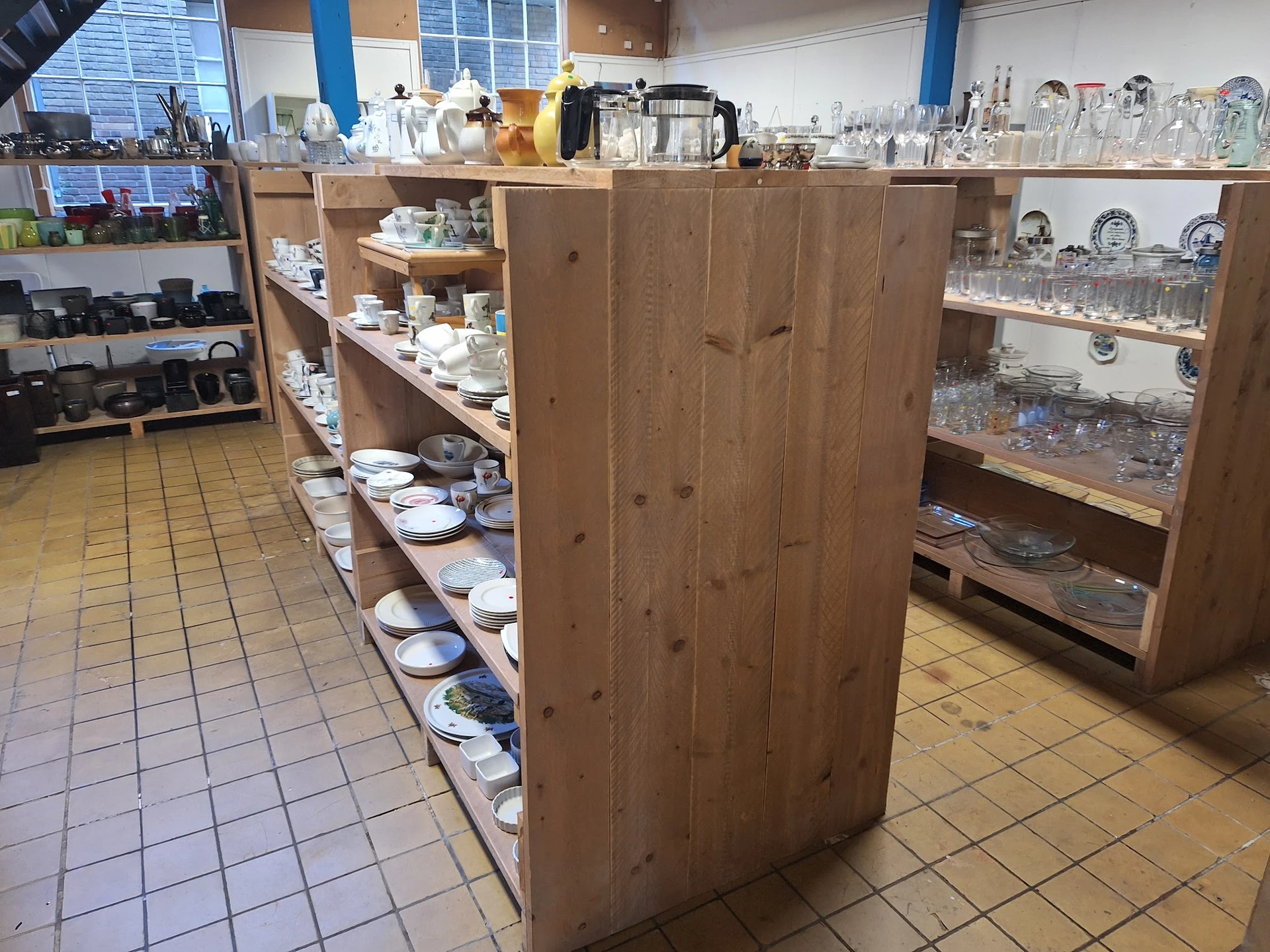 Winkelvloer met houten stellingen vol serviesgoed en huishoudartikelen in kringloopwinkel
