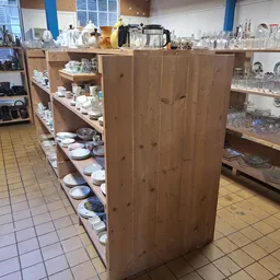 Winkelvloer met houten stellingen vol serviesgoed en huishoudartikelen in kringloopwinkel