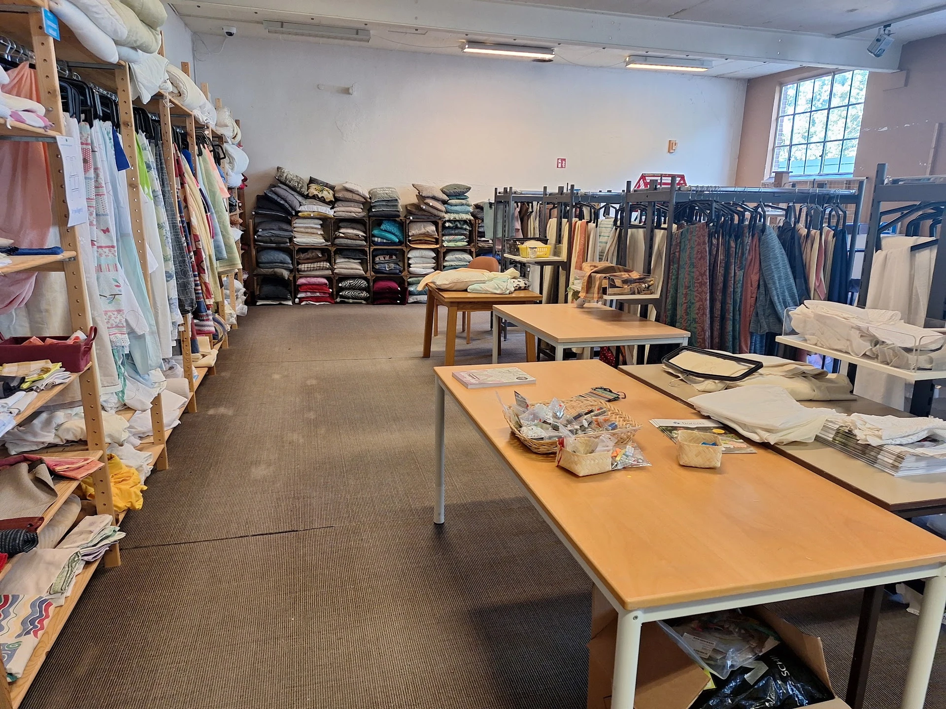 Winkelvloer met werktafels, kledingrekken en stapels textiel in een kringloopwinkel