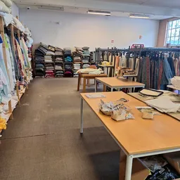Winkelvloer met werktafels, kledingrekken en stapels textiel in een kringloopwinkel