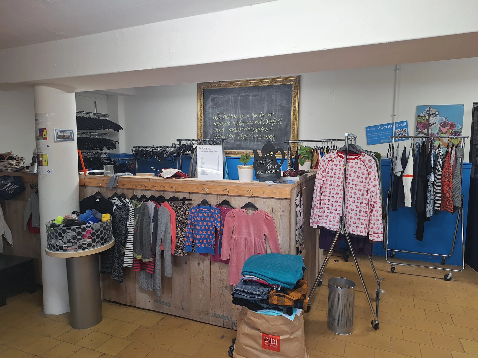 Rekken met tweedehands kinderkleding, waaronder jurken en jasjes in verschillende kleuren en maten