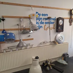 Wandrek met diverse tweedehands huishoudelijke artikelen: lampen, klokken, serviesgoed en decoratie