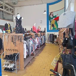 Winkelvloer met houten stellingen vol tweedehands kleding, tassen en accessoires uitgestald