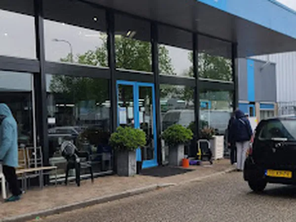 Moderne gevel van kringloopwinkel met grote ramen, blauwe accenten en ingang met plantenbakken