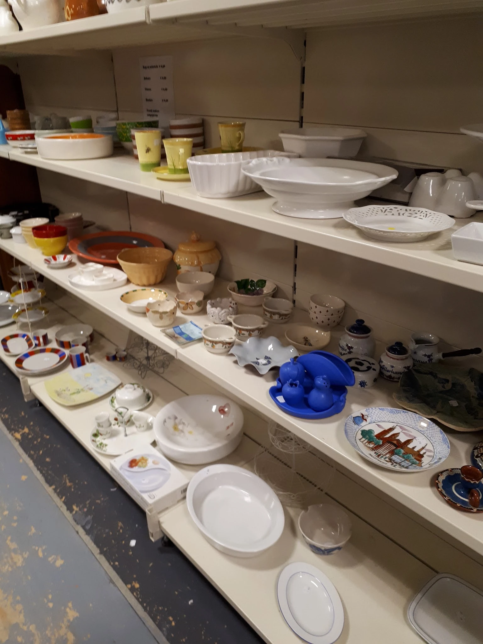Schappen met keramiek, servies, schalen en huishoudelijke artikelen in de kringloopwinkel