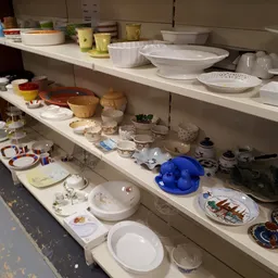 Schappen met keramiek, servies, schalen en huishoudelijke artikelen in de kringloopwinkel