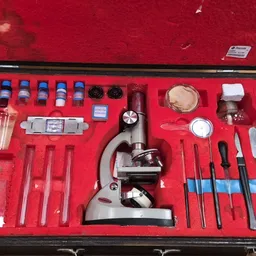 Microscoop in houten koffer met compleet setje accessoires op rode voering