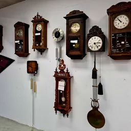 Muur met verzameling van verschillende houten wandklokken, waaronder pendulumklokken en klassieke klokken