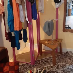 Tweedehands kleding opgehangen aan roze kledingrails en een grijze hoed op een houten stoel