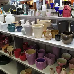 Uitgestalde keramische potten, vazen en plantenbakken in verschillende kleuren en maten op stellingen
