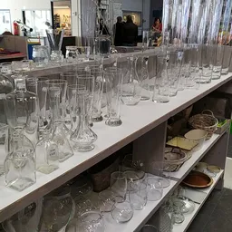 Uitgestalde glaswerk en drinkglazen op witte tafel in kringloopwinkel