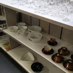 Kastopstelling met serviesgoed: witte en grijze kommen en schalen, donkerbruine kopjes met schotels, en glazen op de bovenste