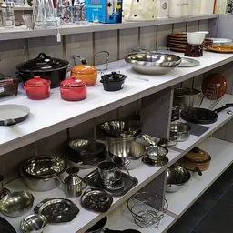 Uitstalling van kookgerei en servies: pannen, potten, schalen en deksel in verschillende kleuren en materialen op twee schapp