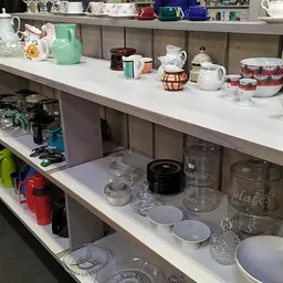 Stellingen met huishoudspullen: serviesgoed, kannen, glazen potten, bekers en decoratieve items