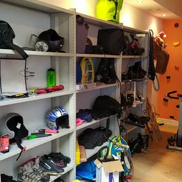 Winkelinterieur met stellingen vol sportartikelen, kleding en fietsaccessoires, oranje muur met klimgrepen en hometrainer op 