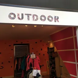 Winkelruit met 'OUTDOOR' opschrift en rood geschilderde wand met uitgestalde jas en sportkleding.