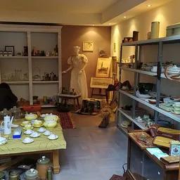 Winkelbinnenruimte met tafels met serviesgoed, stellingen met diverse spullen, een etalagepop en kasttjes.