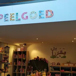 Kleurrijke 'SPELLED' lettersign boven kinderboekenplank in winkel met gele wanden en diverse stellingen